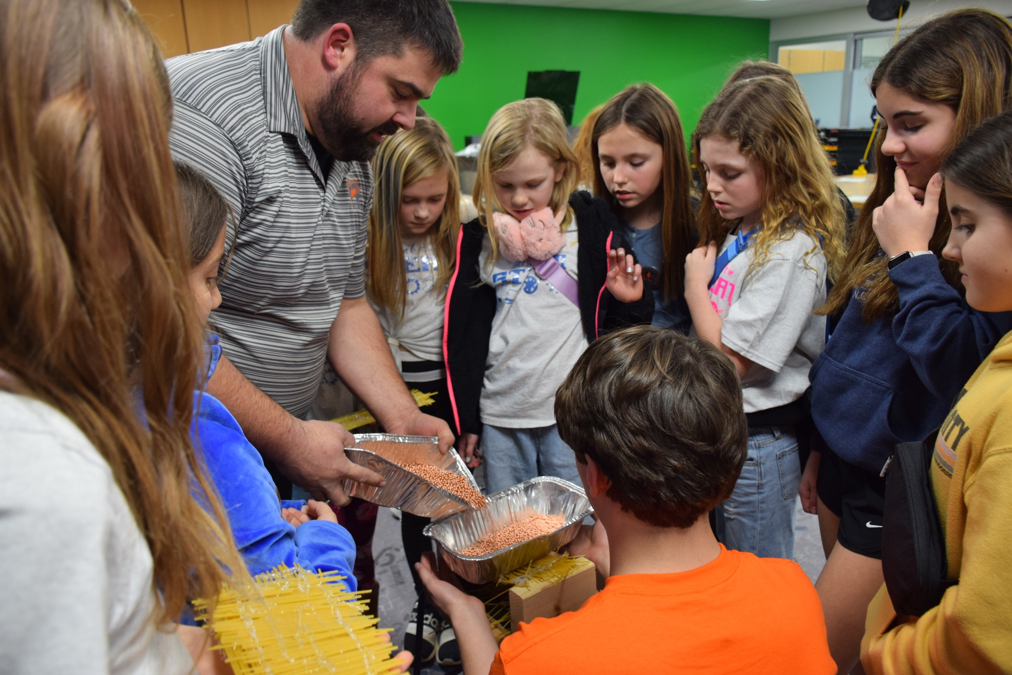Students watching teacher add weight to student-built bridge
